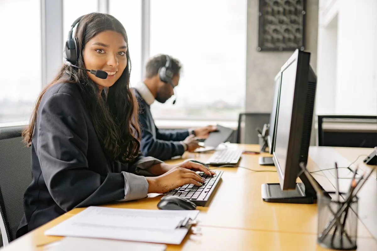 Operadora de call center com headset, sorrindo, em uma mesa de atendimento
